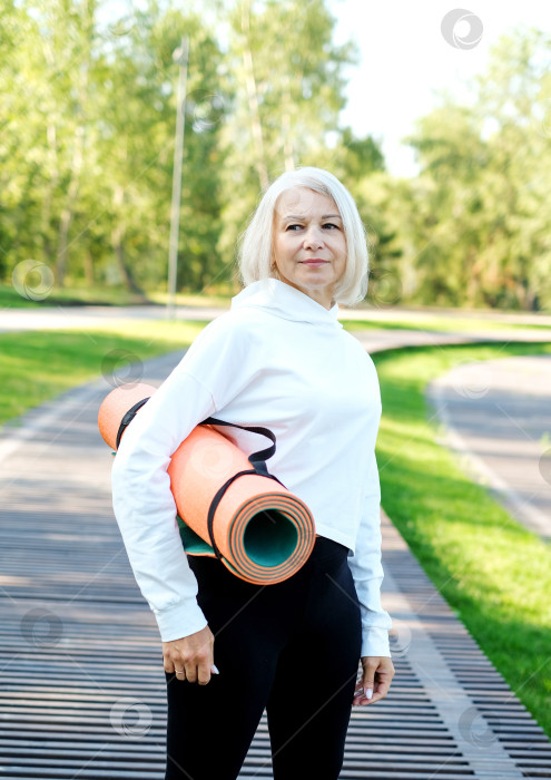 Скачать Йога в парке. Пожилая женщина прогуливается с ковриком для йоги в парке. Концепция здорового активного образа жизни в любом возрасте фотосток Ozero
