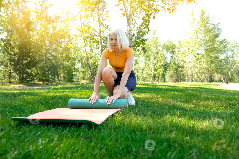 Скачать Йога в парке. Пожилая женщина в позе лотоса сидит на зеленой траве. Концепция спокойствия и медитации. фотосток Ozero