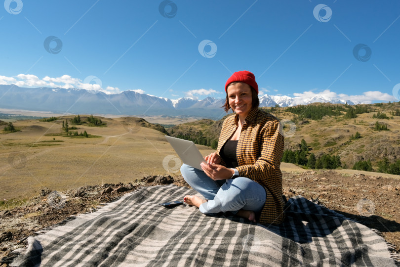 Скачать женщина-путешественница-фрилансер, работающая онлайн с помощью ноутбука и наслаждающаяся прекрасным природным пейзажем с видом на горы. фотосток Ozero