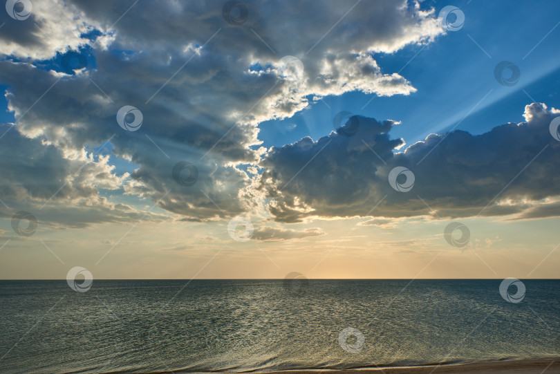 Скачать Закат. Солнечные лучи пробиваются сквозь облака на синем море фотосток Ozero