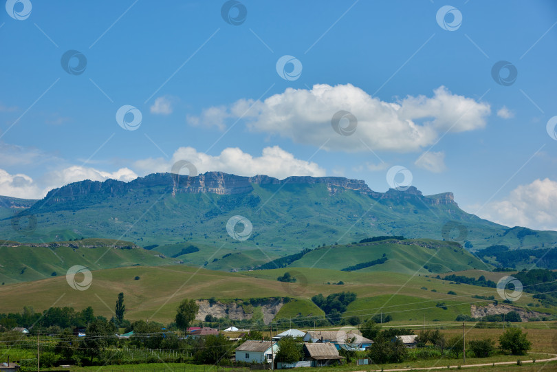 Скачать Маленькая деревушка на фоне горного хребта и голубого облачного неба фотосток Ozero