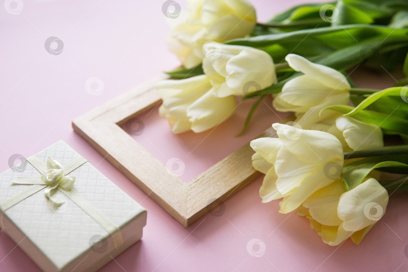 Скачать Желтые цветы тюльпана, фоторамка и подарочная коробка расположены на розовом фоне. Вид сверху, ровный рельеф. Концепция весны. Женский день. фотосток Ozero