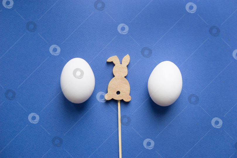 Скачать Пасхальный фон, белые яйца и деревянный заяц на синем фоне, flatlay, вид сверху, пустое место для текста. фотосток Ozero