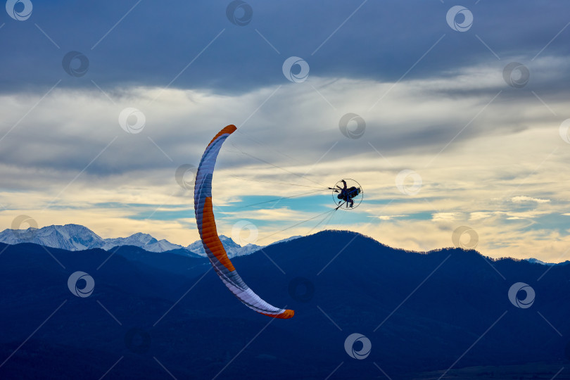 Скачать Экстремальный полет на мотопараплане на фоне грозового неба и заснеженных гор фотосток Ozero