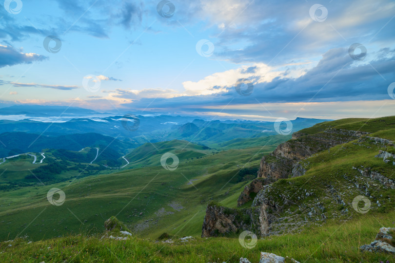 Скачать Кучевые облака на рассвете над зеленой горной долиной с извилистой дорогой и деревней фотосток Ozero