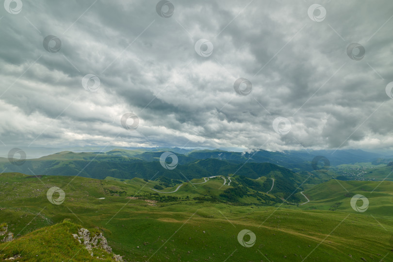 Скачать Грозовые тучи над зеленой горной долиной с извилистой дорогой и деревней фотосток Ozero