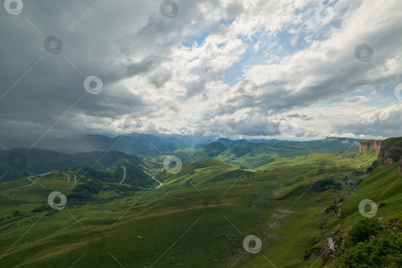 Скачать Грозовые тучи над зеленой горной долиной с извилистой дорогой и деревней фотосток Ozero