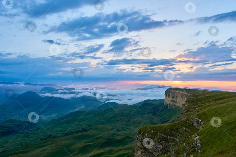 Скачать Облака на закате, голубое небо и туман над горной зеленой долиной с деревней и извилистой дорогой фотосток Ozero