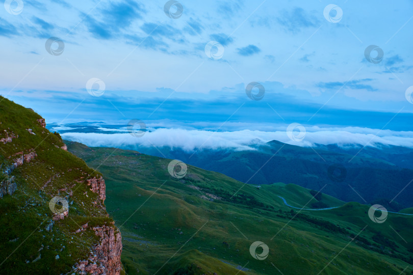 Скачать Облака на закате, голубое небо и туман над горной зеленой долиной с деревней и извилистой дорогой фотосток Ozero