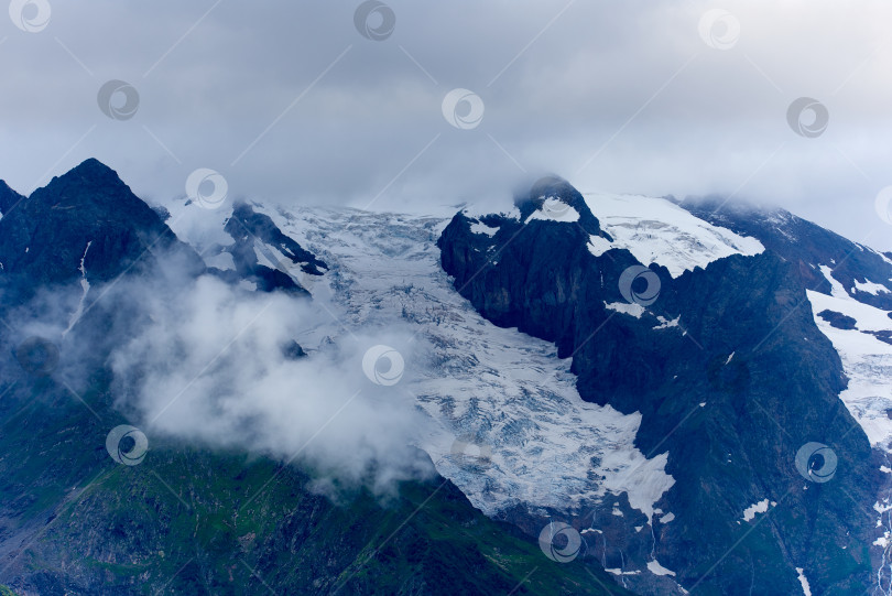Скачать Горный ледник в тумане с зеленой горной долиной внизу. Домбай, Карачаево-Черкесия, Россия фотосток Ozero