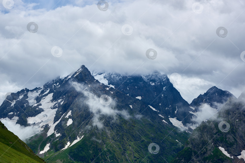 Скачать Скалы, покрытые туманом и облаками, с зелеными склонами. Домбай, Карачаево-Черкесия, Россия фотосток Ozero
