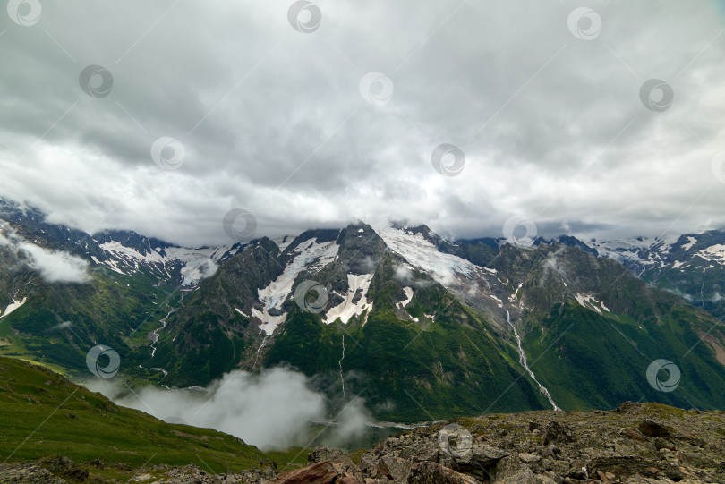 Скачать Горный зеленый хребет, покрытый соснами, в тумане и облаках. Домбай, Карачаево-Черкесия, Россия фотосток Ozero