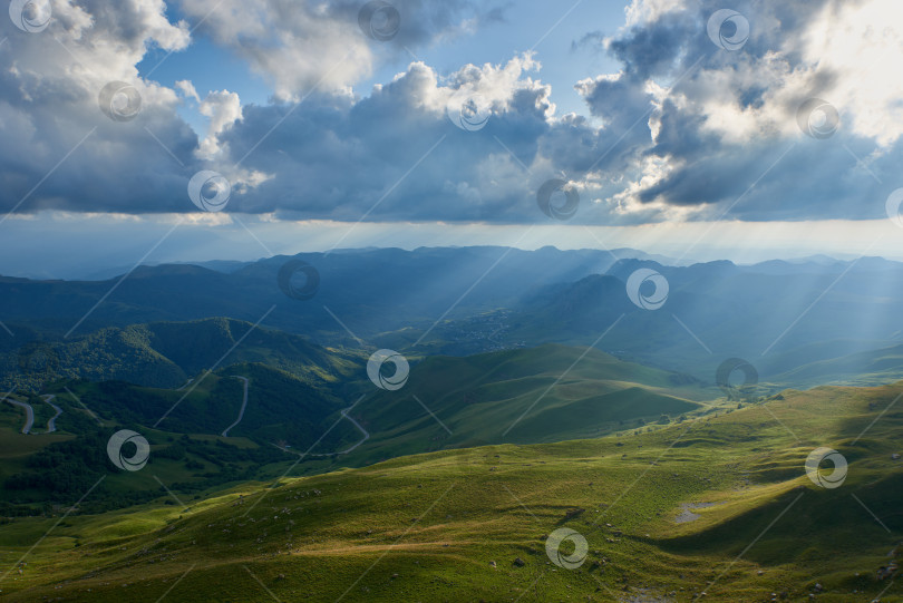 Скачать Солнечные лучи сквозь облака падают на зеленую горную долину. Карачаево-Черкесия, Северный Кавказ, Россия фотосток Ozero