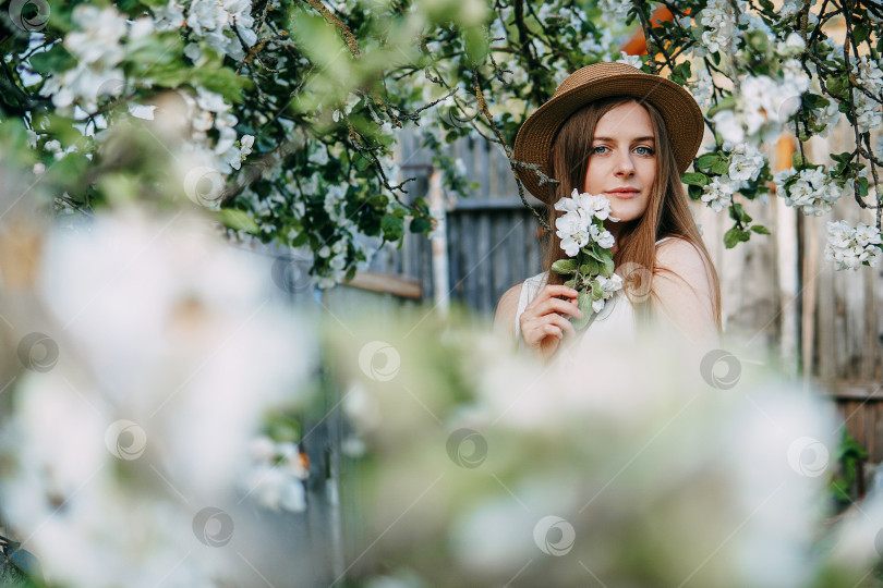 Скачать Красивая молодая девушка в белом платье и шляпке в цветущем яблоневом саду. Цветущие яблони с белыми цветами. фотосток Ozero