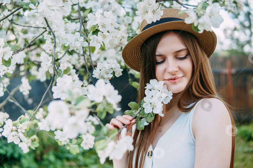 Скачать Красивая молодая девушка в белом платье и шляпке в цветущем яблоневом саду. Цветущие яблони с белыми цветами. фотосток Ozero