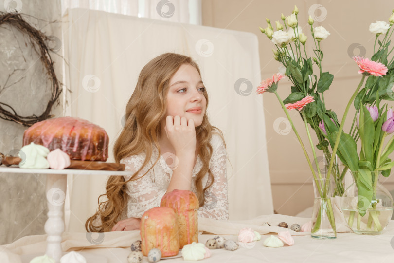 Скачать Девушка с длинными волосами в светлом платье сидит за пасхальным столом с куличами, весенними цветами и перепелиными яйцами. Счастливого празднования Пасхи. фотосток Ozero
