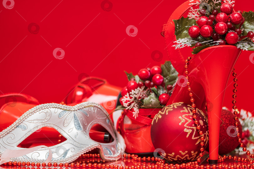 Скачать женские блестящие лакированные красные босоножки на шпильке и новогодние украшения с рождественскими игрушками и карнавальной маской крупным планом на красном фоне фотосток Ozero