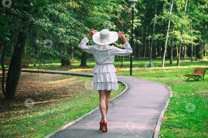 Скачать женщина в коротком летнем платье, широкополой шляпе и туфлях на высоком каблуке утром в парке фотосток Ozero