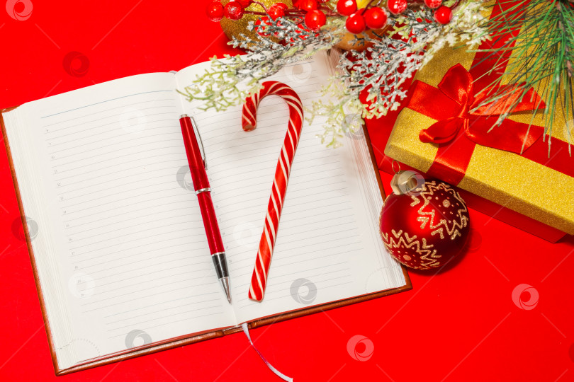 Скачать ручка и леденцовая трость в блокноте на красном столе и рождественские украшения фотосток Ozero
