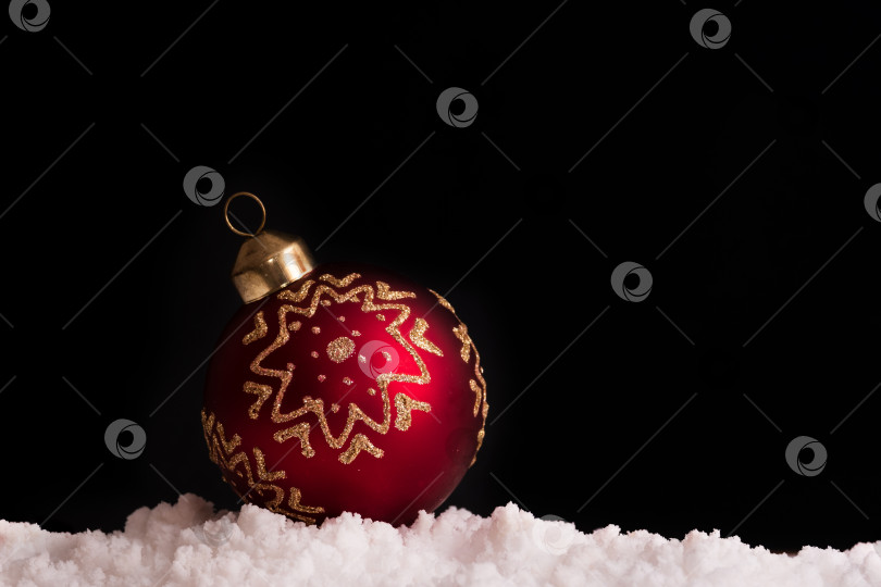 Скачать Рождественский красный шар с золотым орнаментом в снегу на черном фоне фотосток Ozero