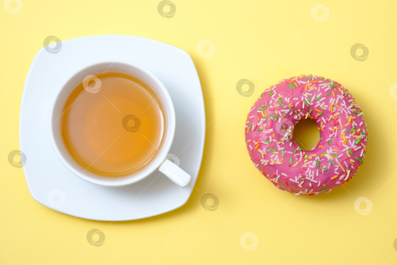 Скачать сладкий пончик с глазурью и чашкой чая на желтом фоне фотосток Ozero
