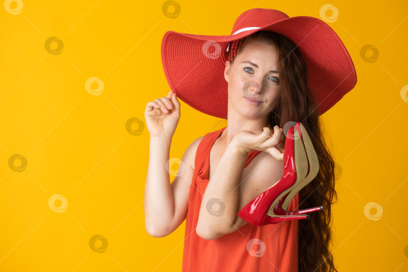 Скачать женщина с длинными волосами в большой красной шляпе и красных туфлях в руке на желтом фоне фотосток Ozero