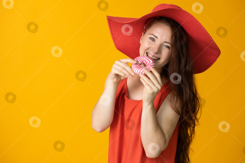 Скачать женщина с длинными волосами в большой красной шляпе и сладким пончиком в руке на желтом фоне фотосток Ozero