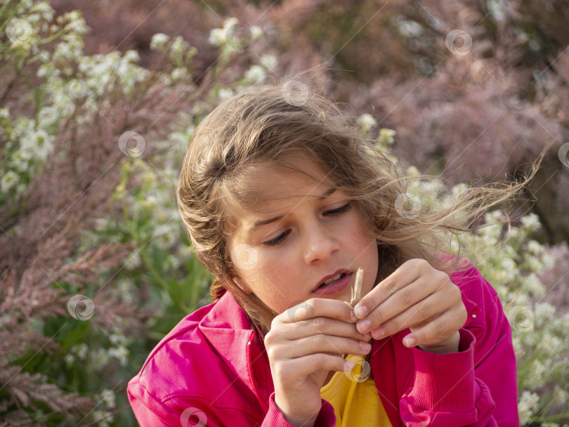 Скачать Симпатичная девочка-подросток задумчиво рассматривает деревянную палку, находясь в весеннем цветущем саду. Красивая девушка держит в руках обломок ветки.Реальная жизнь, естественный свет фотосток Ozero