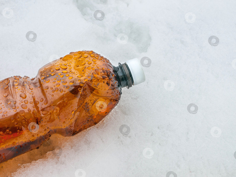 Скачать Пластиковая коричневая бутылка с белой пробкой на снегу, мусор на природе фотосток Ozero