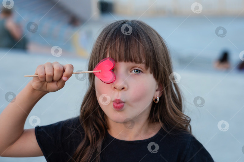 Скачать Забавная маленькая девочка с красным леденцом в форме сердца фотосток Ozero
