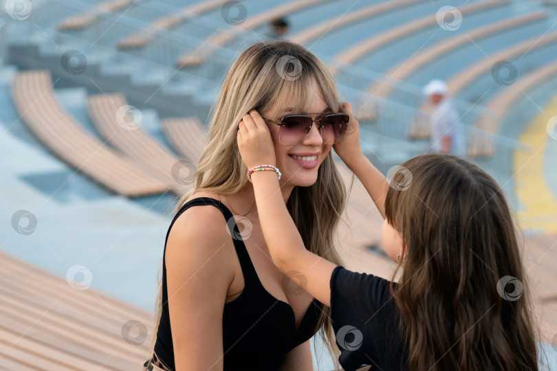 Скачать Маленькая девочка помогает маме надеть солнцезащитные очки на прогулке фотосток Ozero