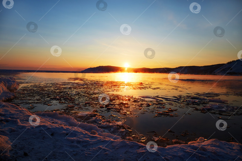Скачать Прекрасный закат на озере Байкал весной. Тающий лед и открытая вода в озере, снег на пляже фотосток Ozero