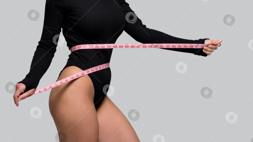 Скачать Стройная женщина в черном боди измеряет талию лентой фотосток Ozero