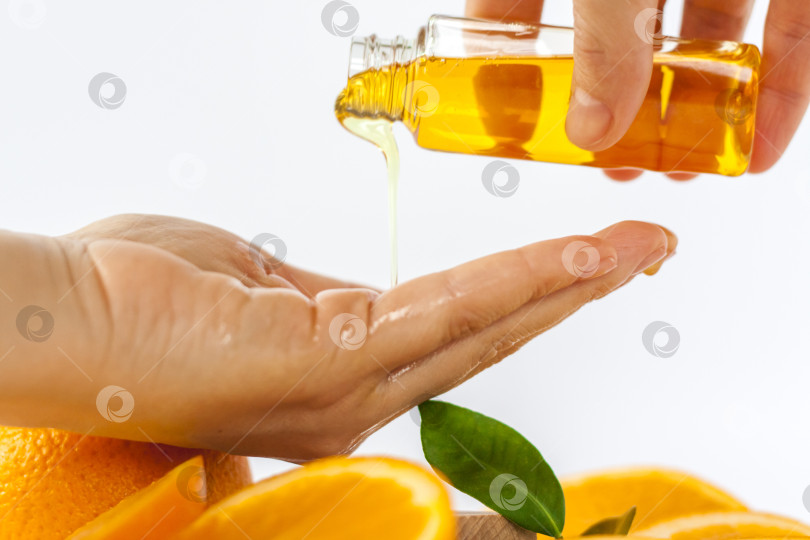 Скачать Апельсиновое масло для тела налейте на ладонь. Нарезанный апельсин на белом фоне. Органическая СПА-косметика с растительными ингредиентами. фотосток Ozero