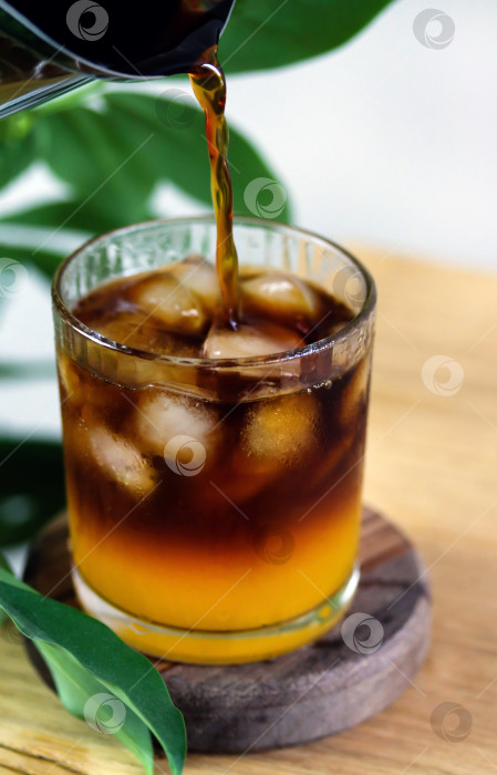 Скачать Готовлю кофе "Шмель". Налейте эспрессо в стакан, наполненный апельсиновым соком, эспрессо, карамельным сиропом и кубиками льда. Модный кофейный напиток, многослойный кофейный коктейль на деревянном столе, крупным планом фотосток Ozero