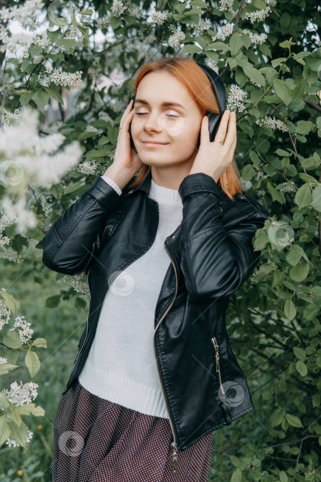 Скачать Рыжеволосая девочка-подросток слушает музыку в наушниках, настроенных с помощью телефона. Время весеннего цветения вишневых садов фотосток Ozero