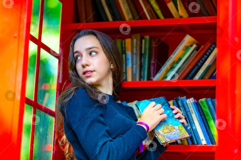 Скачать Молодая девушка-подросток берет книгу для чтения в библиотеке, чтобы учиться и готовиться к экзаменам в университет или колледж. фотосток Ozero