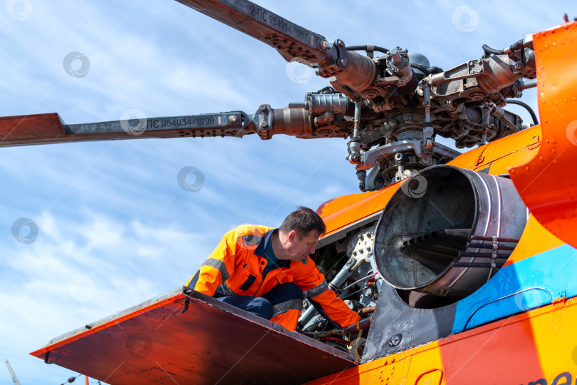 Скачать Техник - наземный персонал в аэропорту проверяет двигатель вертолета. Снимок сделан с подсветкой и солнечными бликами.  Техническое обслуживание вертолета. фотосток Ozero