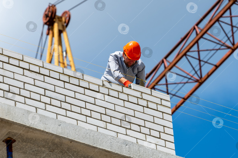 Скачать Череповец, Россия, 24 июня 2022 года рабочий-строитель возводит кирпичную стену на строительной площадке нового дома. Кирпичная кладка, строитель кладет кирпич. фотосток Ozero