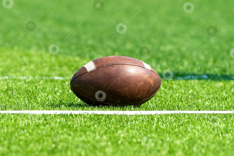 Скачать Мяч для американского футбола на фоне зеленого травянистого поля рядом с белой линией. Тренировка по регби в колледже. фотосток Ozero