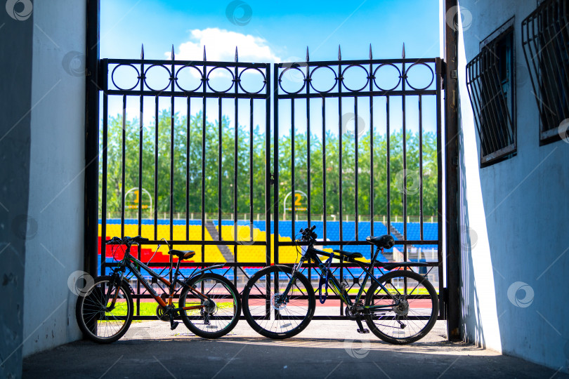 Скачать Череповец, Россия, 25 июня 2022 года Силуэты велосипедов в городе, стоящих у железных ворот стадиона. Концепция здорового образа жизни и езды на велосипеде. фотосток Ozero
