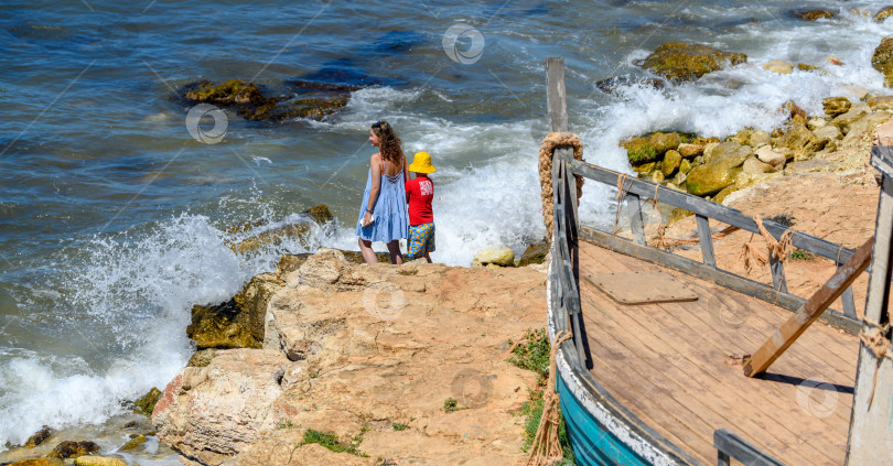 Скачать Севастополь, Крым, 18 июля 2022 года Мать со своим маленьким сыном стоят на скалистом морском берегу. Мама с ребенком, летние каникулы на море. фотосток Ozero