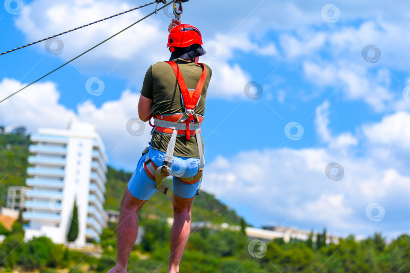 Скачать Мужчина спускается по металлическому тросу в альпинистском снаряжении. Зиплайн - это экстремальный вид развлечения на природе, в городском парке и в горах. фотосток Ozero