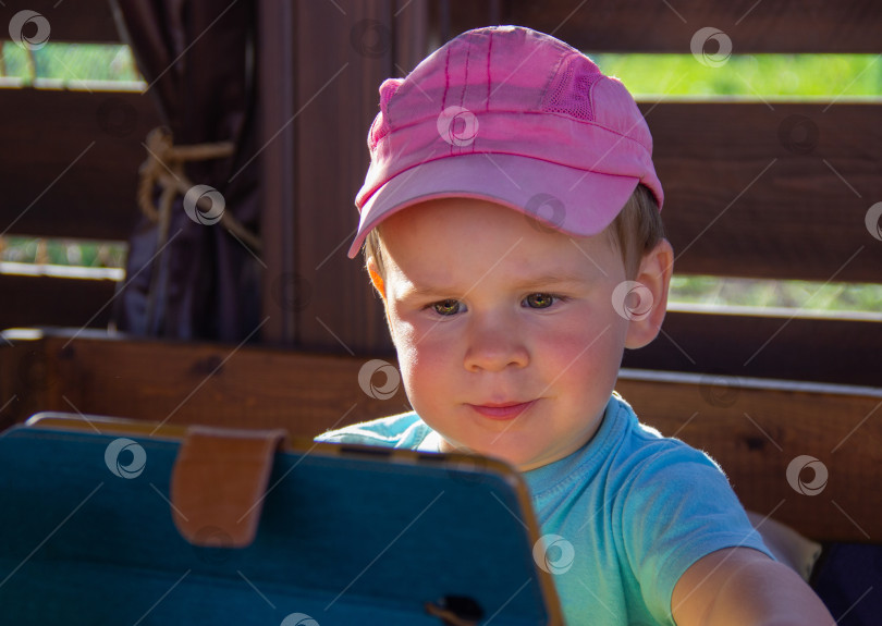 Скачать малыш внимательно смотрит на экран смартфона. Ребенок очарован играми и приложениями на телефоне. Юный геймер фотосток Ozero