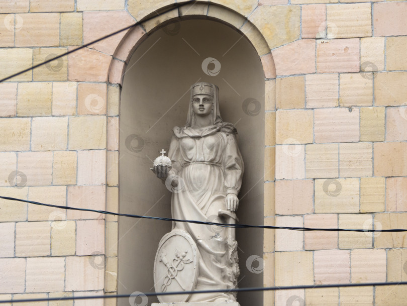 Скачать Старая статуя в нише кирпичного здания. Скульптура женщины, обладающей силой и мечом в руках, имеет щит у ее ног. Провода проходят по переднему плану. Архитектурный памятник фотосток Ozero