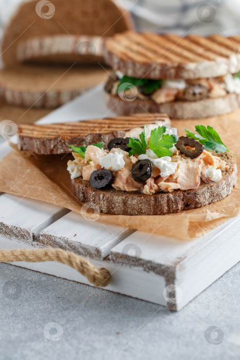 Скачать Бутерброд с запеченной рыбой (тунцом или лососем) с маслинами, сыром Фета и петрушкой на ржаном хлебе. Средиземноморский завтрак с морепродуктами.   Избирательный фокус фотосток Ozero