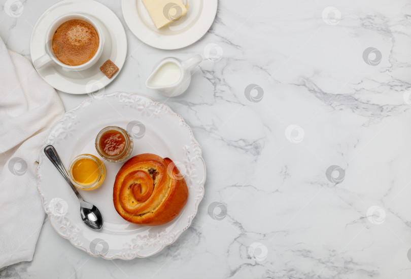 Скачать Сладкая булочка с изюмом, джемом и медом на белой тарелке на мраморном фоне на завтрак. Кофе, молоко, масло на столе. Выборочный фокус, вид сверху и пространство для копирования фотосток Ozero