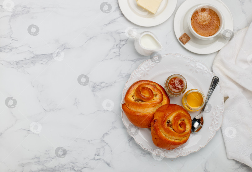 Скачать Две булочки с изюмом, джемом и медом на белой тарелке на мраморном фоне на завтрак. Кофе, молоко, масло на столе. Выборочный фокус, вид сверху и пространство для копирования фотосток Ozero