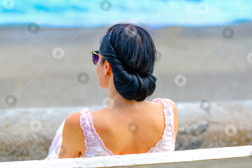 Скачать Молодая брюнетка сидит в одиночестве на скамейке у моря и расслабляется, наслаждаясь отдыхом. фотосток Ozero