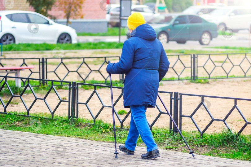 Скачать Активная пожилая женщина тренируется в скандинавской ходьбе. Прогулка пенсионера. фотосток Ozero